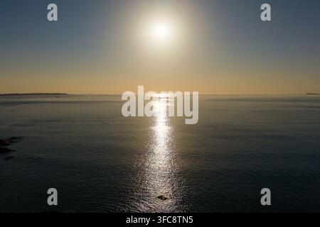 Lumière dorée du soleil du soir se reflétant sur la surface calme de l'océan au coucher du soleil, houle douce sur la mer avec un promontoire lointain à l'horizon sous un ciel crépusculaire clair Banque D'Images