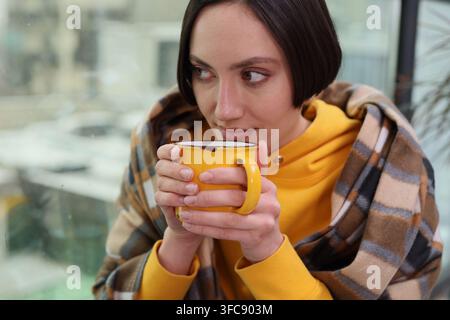Une jolie brune profite d'une pause thé chaud en se reposant près de la fenêtre Banque D'Images