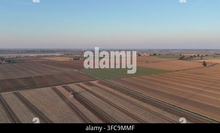 Vue aérienne des terres cultivées dans le val de la Po, mettant en valeur des cultures variées et des activités agricoles avec un tracteur en action Banque D'Images