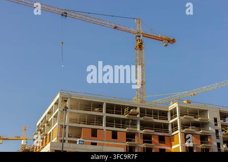 Un bâtiment en béton à plusieurs étages inachevé avec des sections de briques apparentes et plusieurs grues de tour se dresse contre un ciel bleu clair. Le regard tourné vers le haut Banque D'Images