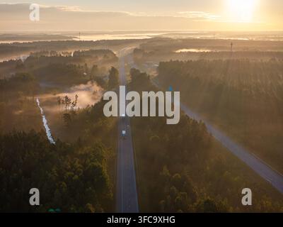 Vue aérienne de l'autoroute A2 E77 près de Sigulda, Lettonie au lever du soleil avec circulation, brume matinale et lumière dorée Banque D'Images