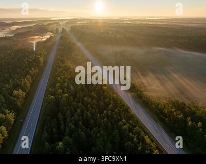 Vue aérienne de l'autoroute A2 E77 traversant des forêts et des champs brumeux près de Sigulda, Lettonie, au lever du soleil Banque D'Images