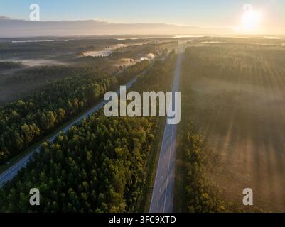 Vue aérienne de l'autoroute A2 E77 traversant une forêt et un paysage brumeux près de Sigulda, Lettonie, au lever du soleil Banque D'Images