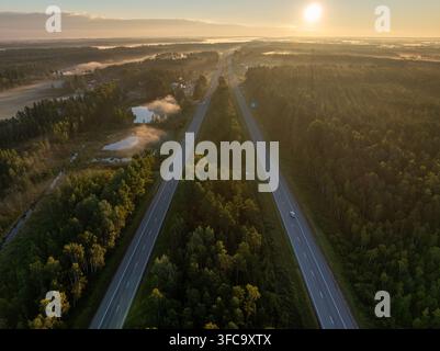 Vue aérienne de l'autoroute A2 E77 près de Sigulda, Lettonie au lever du soleil avec circulation, forêt et brume matinale Banque D'Images