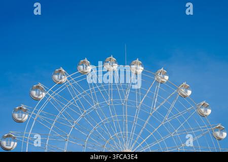 L'arc supérieur d'une grande roue blanche géante avec des capsules rondes se détache sur un ciel bleu clair et lumineux. Banque D'Images