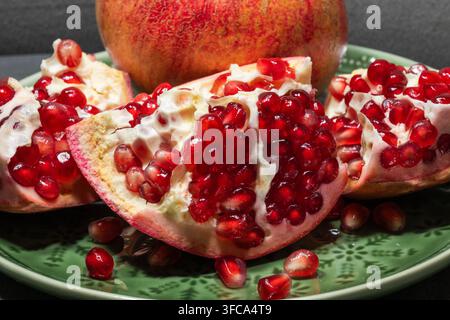 Une prise de vue en gros plan montre une grenade mûre coupée en sections, révélant ses arilles rouges vives sur une assiette verte. Banque D'Images