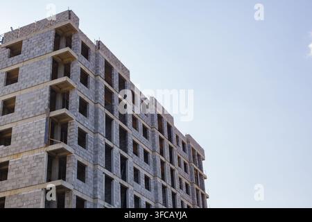 Vue en contre-plongé d'un bâtiment résidentiel à plusieurs étages en cours de construction, fait de blocs de béton, contre un ciel bleu clair, offrant un espace de copie généreux pour ur Banque D'Images