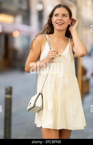 Jeune femme en robe d'été regarde les cafés de rue tout en marchant dans la rue de la ville Banque D'Images