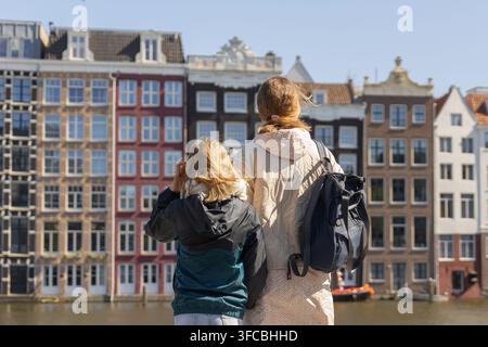 Une mère et sa fille se tiennent ensemble près d'un canal à Amsterdam. Elles regardent les bâtiments colorés et profitent de leur temps en voyageant en Europe. Banque D'Images