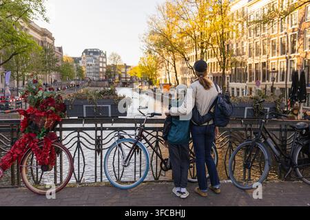 Mère et fille se tiennent au bord du canal à Amsterdam, observant l'eau et les bâtiments. Elles profitent de leur temps ensemble en vacances. Banque D'Images