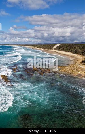 Vue aérienne verticale de la pointe escarpée et de la côte rocheuse de Brooms Head avec le long rivage sablonneux de Sand Dune Beach, océan Pacifique et surfeur Banque D'Images