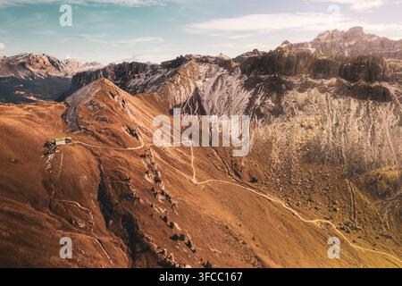 Vue aérienne de Schluterhutte nichée sur les pentes abruptes des Dolomites avec des sentiers de montagne sinueux, des sommets rocheux et une lumière dorée d'automne à Funes Banque D'Images