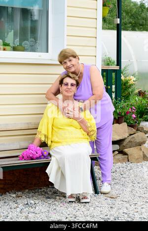 Portrait authentique de deux sœurs russes âgées de 80 et 75 ans assises sur un banc près d’un porche de maison dans un jardin d’été en Russie Banque D'Images