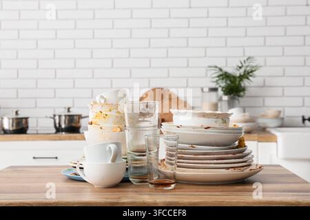 Ménage et désordre dans la cuisine, une pile de vaisselle et de verres sales sur une table en bois dans une cuisine moderne Banque D'Images