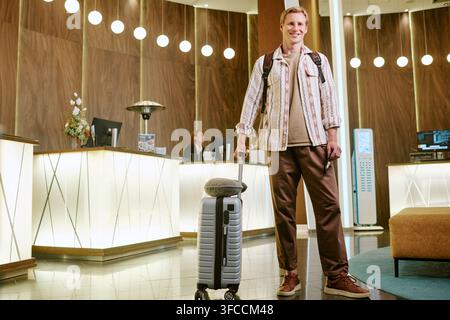 Portrait d'un homme souriant debout avec une valise dans le hall d'hôtel Banque D'Images