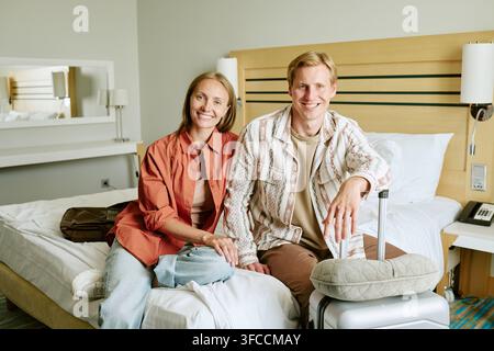 Portrait d'un couple souriant assis sur un lit d'hôtel en vacances Banque D'Images
