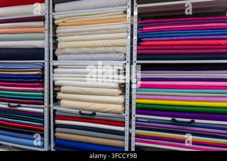 Rouleaux de tissu empilés sur des étagères dans un magasin de tissus et de textiles présentant diverses couleurs et textures Banque D'Images