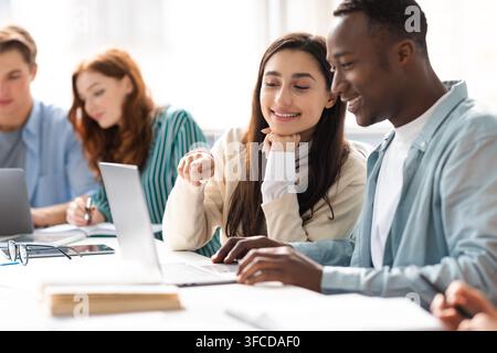 Éducation et travail d'équipe. Des étudiantes et des hommes souriants, assis à leur bureau dans la bibliothèque publique, parlent, font leurs devoirs ou font des groupes Banque D'Images