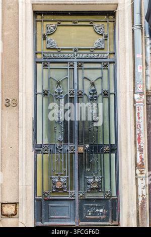 Une porte en fer forgé de style Art Nouveau ornée de volutes florales et de panneaux en verre dépoli marque l’entrée à côté de la Pharmacie du Ginkgo au numéro 38 Rue des Dominicains à Nancy, Grand Est, France. Un tuyau d’évacuation patiné court à côté, épousant la façade en grès. Banque D'Images