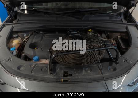 Capot ouvert avec compartiment moteur exposé attendant l'inspection de service dans l'atelier. Le ventilateur de refroidissement, les réservoirs de liquide et la batterie sont bien visibles sous le capot relevé Banque D'Images