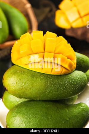 Demi-mangue coupé en dés posée sur des mangues vertes entières avec un fond flou. Banque D'Images