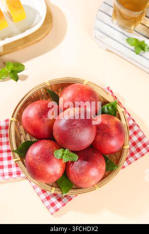 Des nectarines fraîches dans un panier en bambou sur une nappe à carreaux, vue de dessus. Banque D'Images