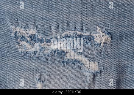 Close up de jeans bleu clair usés montrant des pièces de tissu déchirées et des fils blancs lâches Banque D'Images