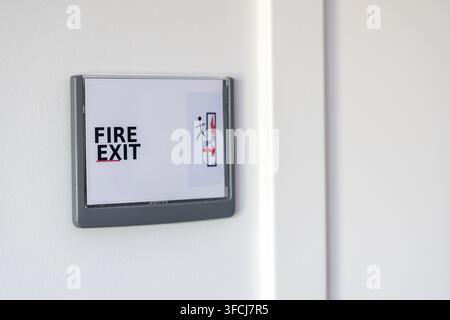 Un panneau de sortie de secours clair avec du texte et un pictogramme d'une personne en course est fixé sur un mur blanc uni Banque D'Images