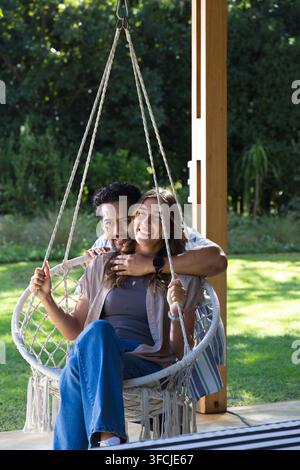 Couple divers assis sur une chaise suspendue en macramé sur la véranda de l'arrière-cour tenant des cordes tressées Banque D'Images