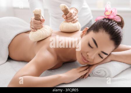 Femme asiatique détendue ayant la balle de fines herbes comprimez la séance de massage du dos dans le spa Banque D'Images