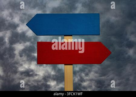 Panneaux flèches en bois bleu et rouge vierges contre un ciel orageux. Deux panneaux indicateurs en bois vides en rouge et bleu pointant dans des directions opposées. Concept de c Banque D'Images