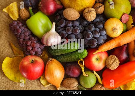 Vue de dessus en gros plan d'une riche récolte automnale mettant en avant des fruits bio frais, des légumes et des noix disposés sur un fond en toile de jute rustique. Banque D'Images