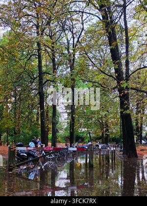 Une zone de stationnement inondée et une piste cyclable avec des arbres reflétés dans l'eau profonde après une forte tempête de pluie automnale. Banque D'Images