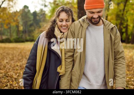 Couple heureux marchant ensemble dans un parc automnal couvert de feuilles dorées Banque D'Images