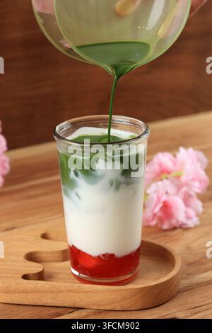 Verser le Matcha dans le verre avec de la confiture de fraises et du lait. Procédé de fabrication du latte au matcha et fraises Banque D'Images