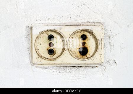 Une ancienne prise brûlée dans le mur. Prise sale dans le mur de plâtre blanc. Banque D'Images