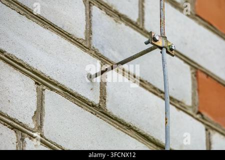 Macro d'un câble électrique endommagé avec conducteurs en cuivre exposés suspendu à l'extérieur près d'un vieux mur de briques blanches. Banque D'Images