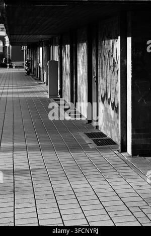 Passage couverte urbaine avec murs de briques couverts de graffitis et une forte perspective géométrique en noir et blanc Banque D'Images