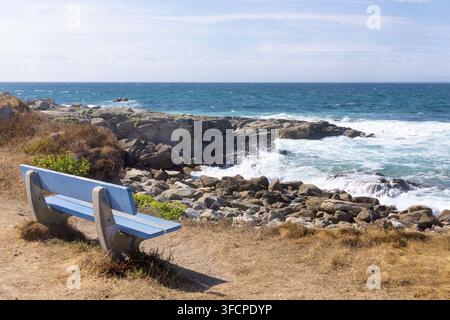 Un banc en bois bleu vide à côté du sentier côtier surplombant les vagues se brisant sur la côte rocheuse à Penmarc'h, Finistère, Bretagne, France. Banque D'Images