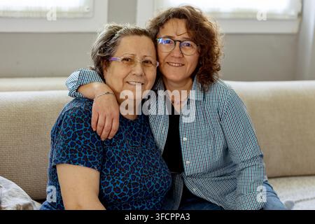 Fille adulte heureuse embrassant sa mère âgée sur un canapé Banque D'Images