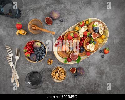 Arrangement de petit-déjeuner en hauteur mettant en vedette des crêpes, des baies, des figues et des garnitures de fruits sur une table rustique Banque D'Images