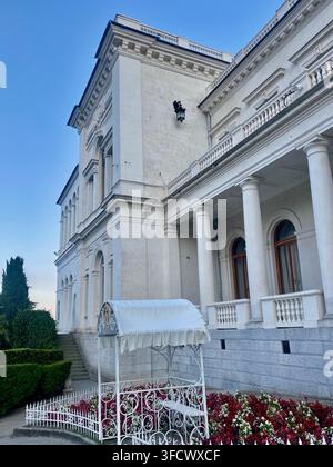 Yalta, Russie - 17 juillet 2022 : Élégante façade de palais blanc avec colonnes classiques et jardin paysagé en Crimée. Banque D'Images