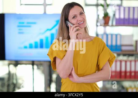 Femme d'affaires souriante parlant au smartphone pendant une pause au bureau Banque D'Images