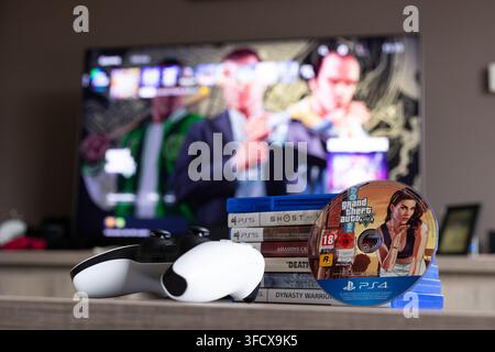 BRECHT, BELGIQUE – 28 août 2026 : Portrait rapproché d'une pile de jeux PS5, d'une manette, d'un disque physique de jeu PlayStation de GTA et d'une maison floue Banque D'Images