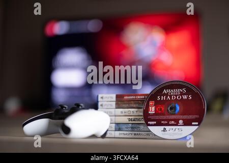 BRECHT, BELGIQUE – 28 août 2026 : Portrait rapproché d'une pile de jeux PS5, d'une manette, d'un disque de jeu physique et d'un écran d'accueil PlayStation flou Banque D'Images