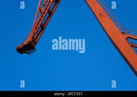 Demi-lune dans un ciel bleu clair encadrée par la structure en acier rouge d'une grue portuaire massive, prise de vue en contre-plongée Banque D'Images