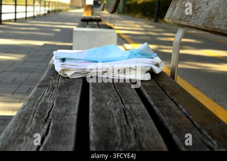 Des chiffons de couleur claire pliés reposent sur un banc en bois patiné à côté d'une allée pavée bordée d'une ligne jaune. Une lumière chaude du soleil crée de longues ombres, tandis que Banque D'Images