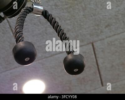 Une vue rapprochée inclinée d'un accessoire de corde pour triceps suspendu à une station de machine à câble. L'image montre la corde en nylon noir torsadée, la connexion métallique Banque D'Images