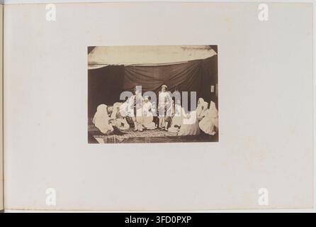 Un groupe de personnes en tenue traditionnelle, assises en demi-cercle sous une structure semblable à une tente, dans une photographie de Félix-Jacques-Antoine Moulin, photographe français, prise dans la province d'Alger, en Algérie, entre 1856 et 1857. Banque D'Images