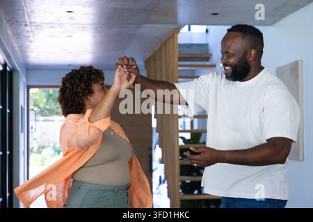 Couple afro-américain dansant dans le couloir près des escaliers en bois, homme en tee-shirt blanc, femme portant de l'orange Banque D'Images